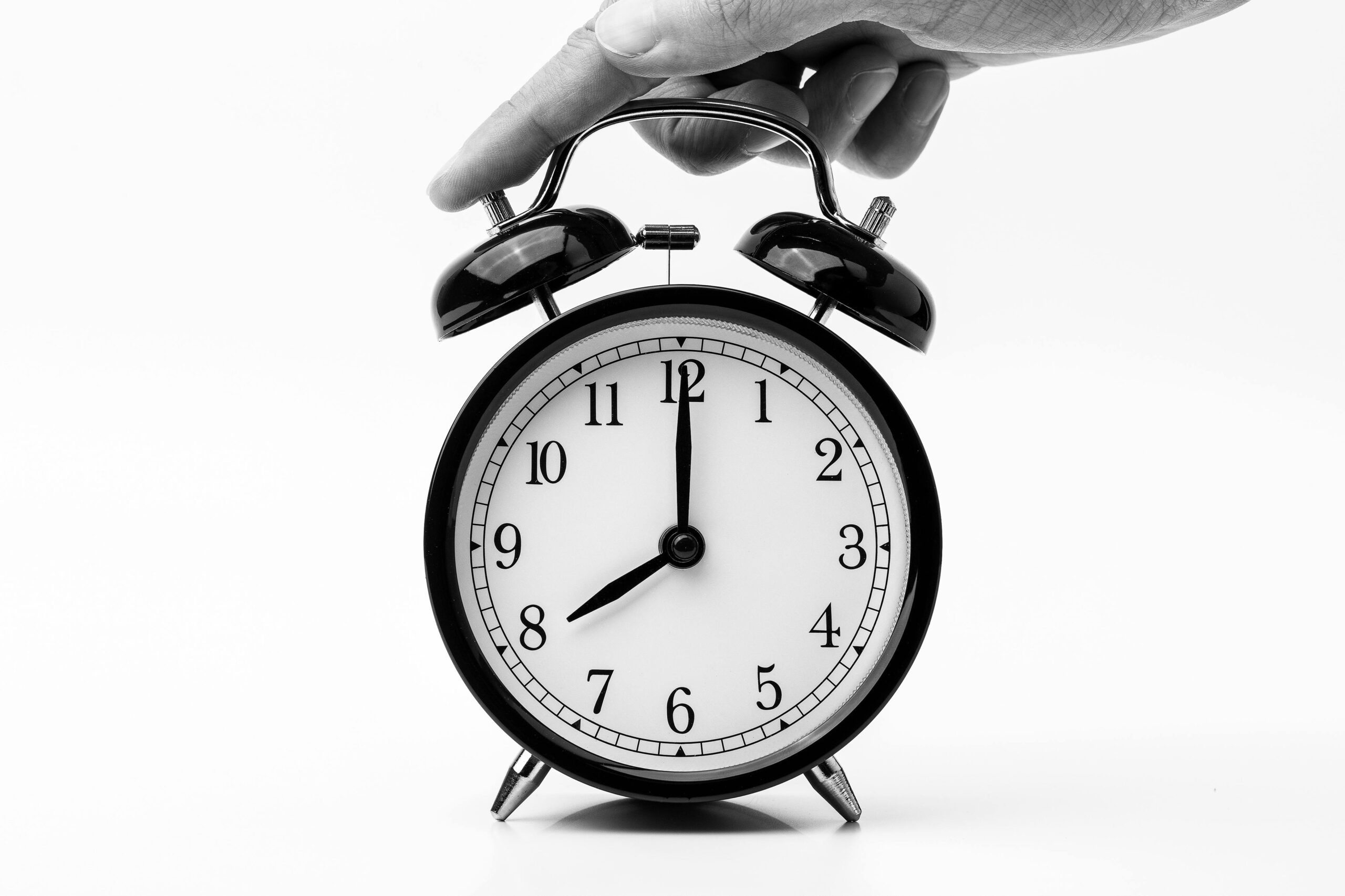 A classic black and white alarm clock being held by a hand, depicting the concept of time.